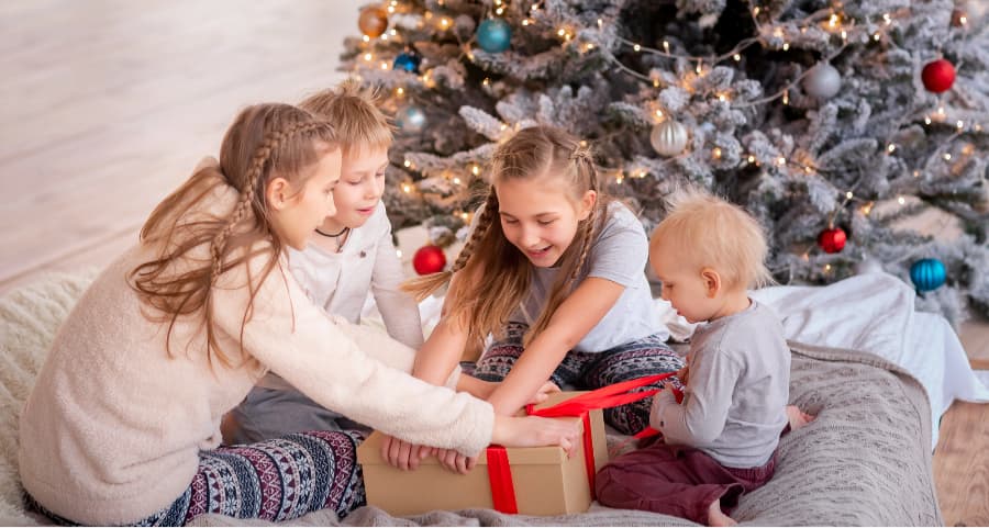 Children opening a gift in the living room near a Christmas tree.